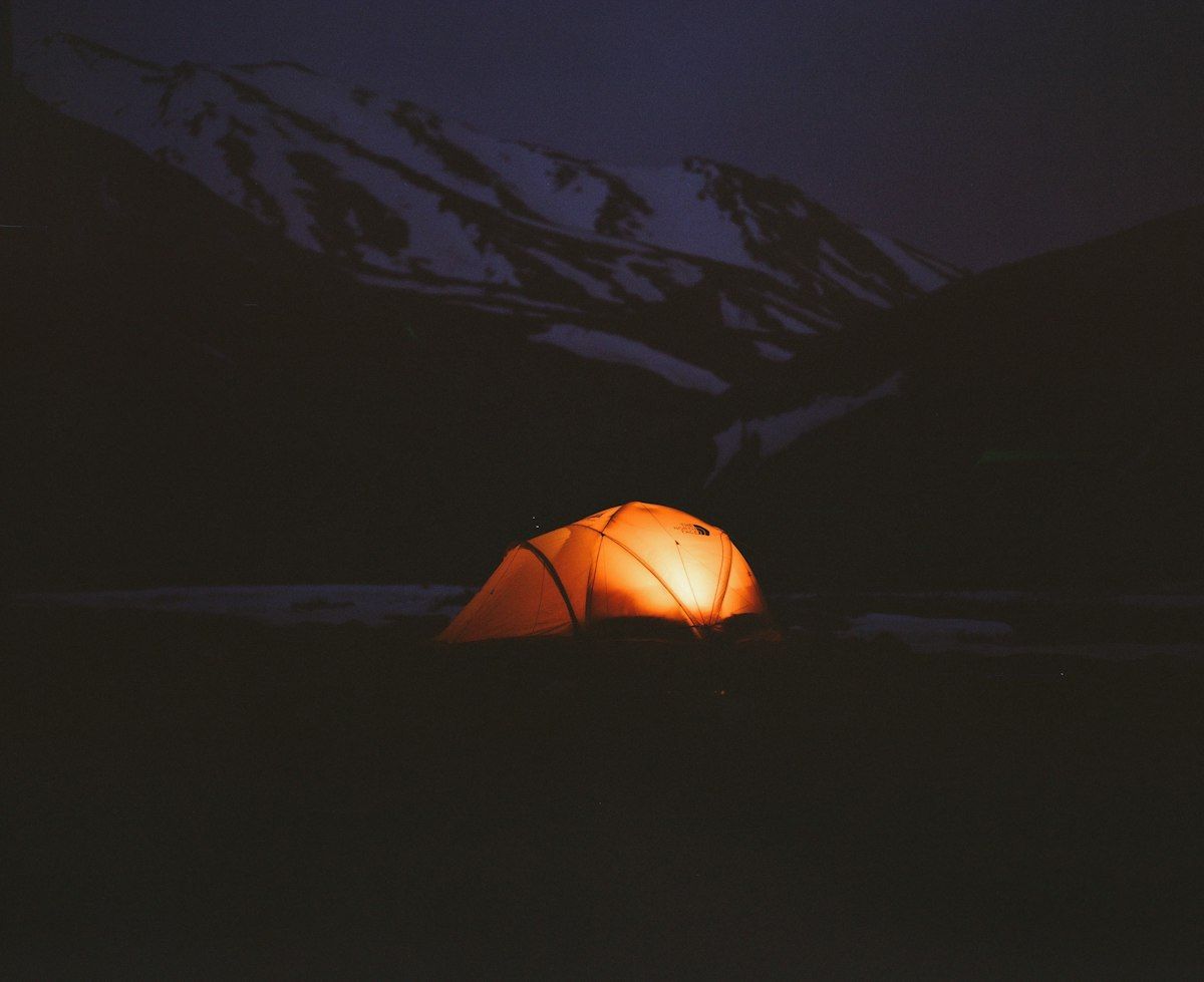 Lit tent at night below dark mountains