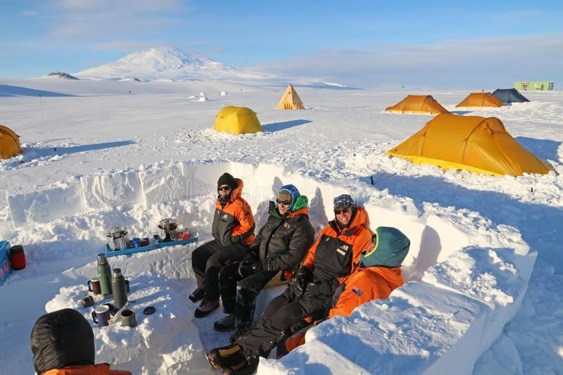 Expedition members in a snow kitchen beside tents
