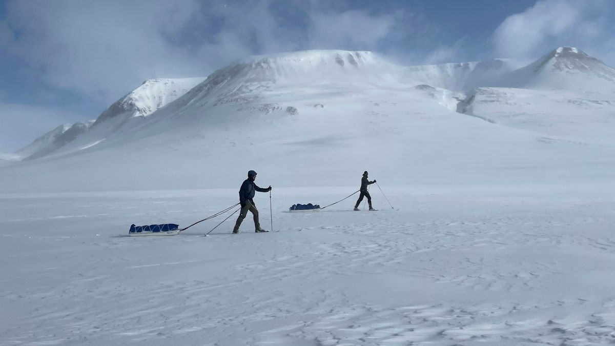 Two skiers hauling sleds across a snowfield