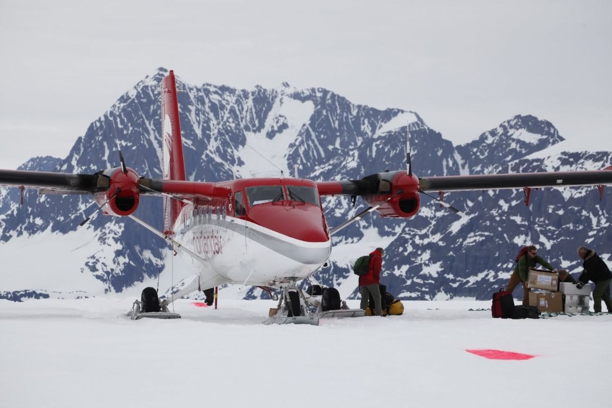 Twin-engine ski plane on the ice with crew unloading