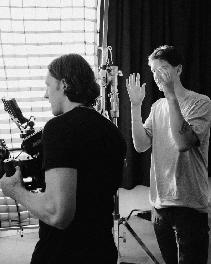 Two crew members laughing beside a camera, black and white