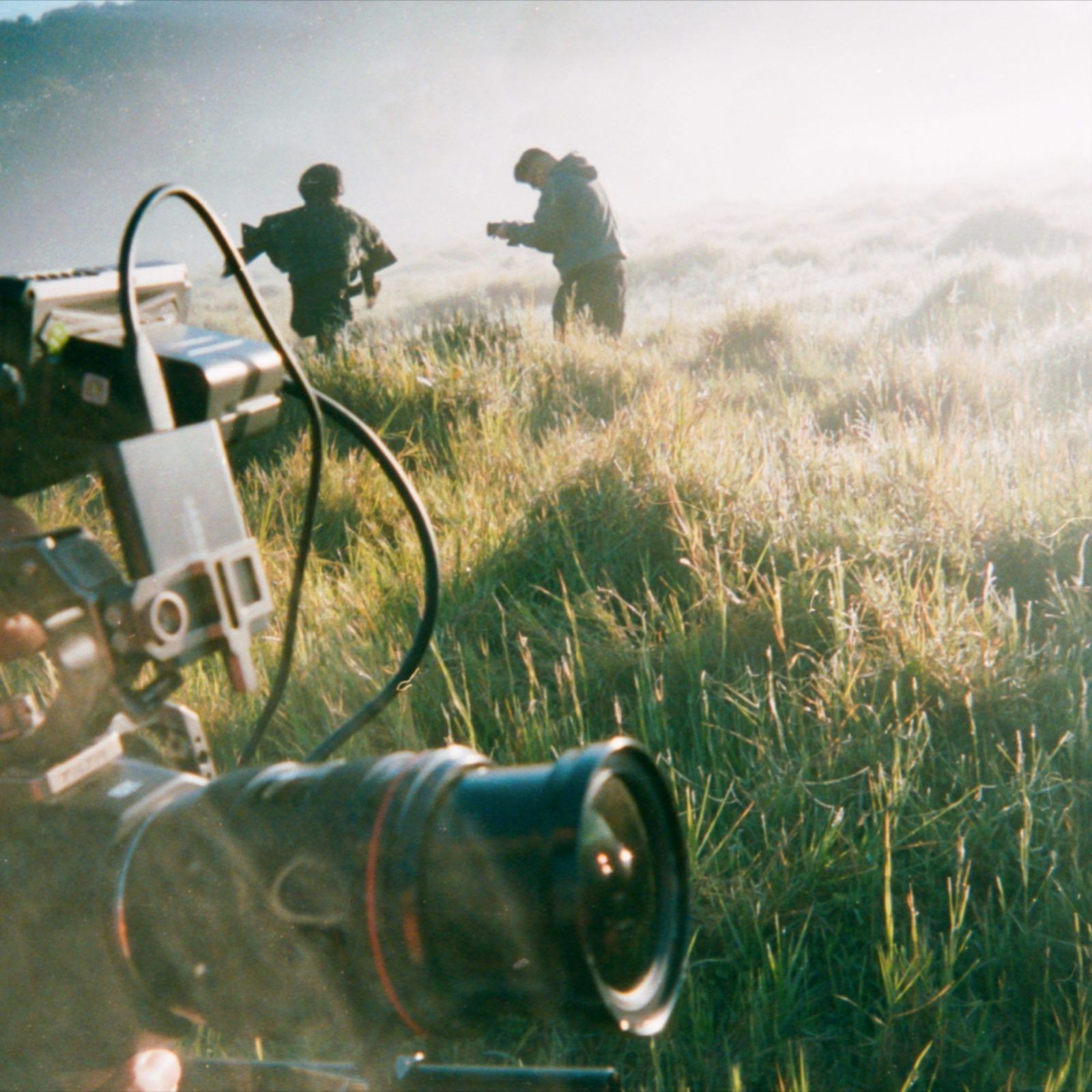 Cinema camera in long grass with crew on the ridge behind