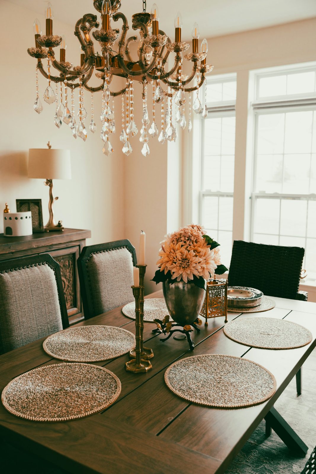 Dining table set with woven placemats under a crystal chandelier