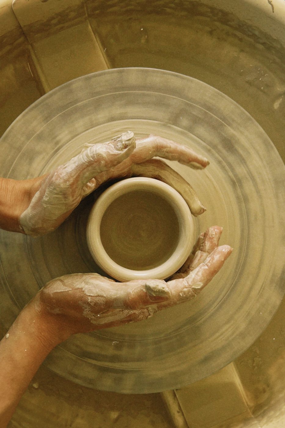 Hands centring clay on a wheel, seen from above