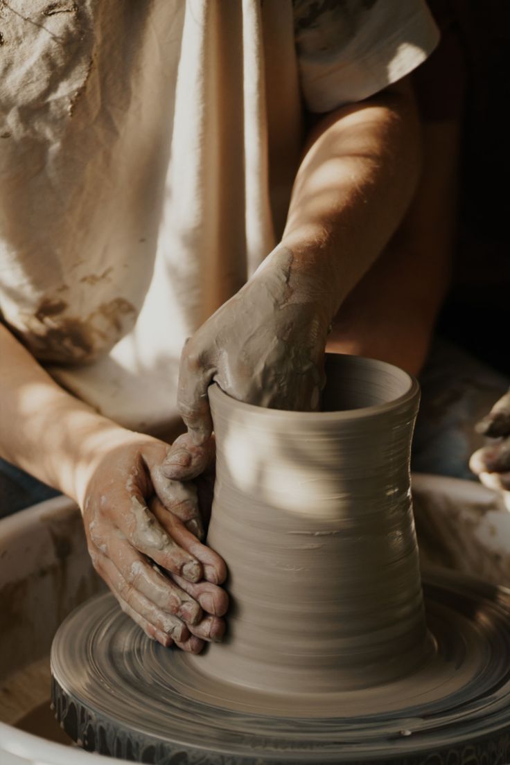Hands pulling up a clay cylinder
