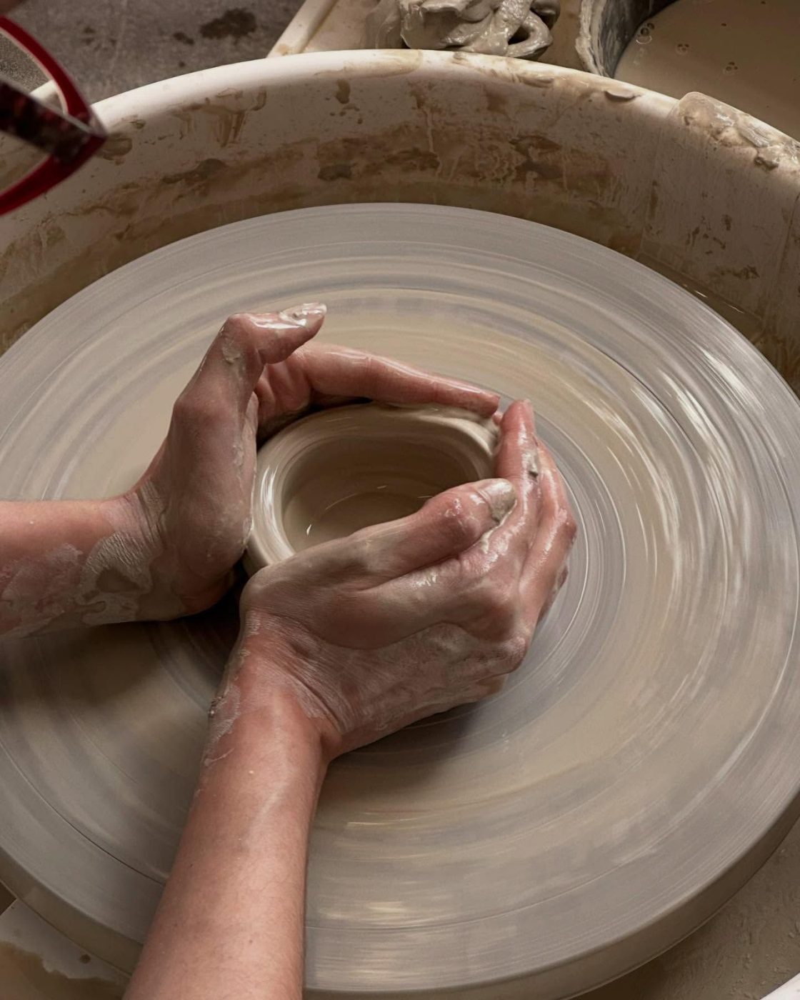 Hands opening a pot on the wheel