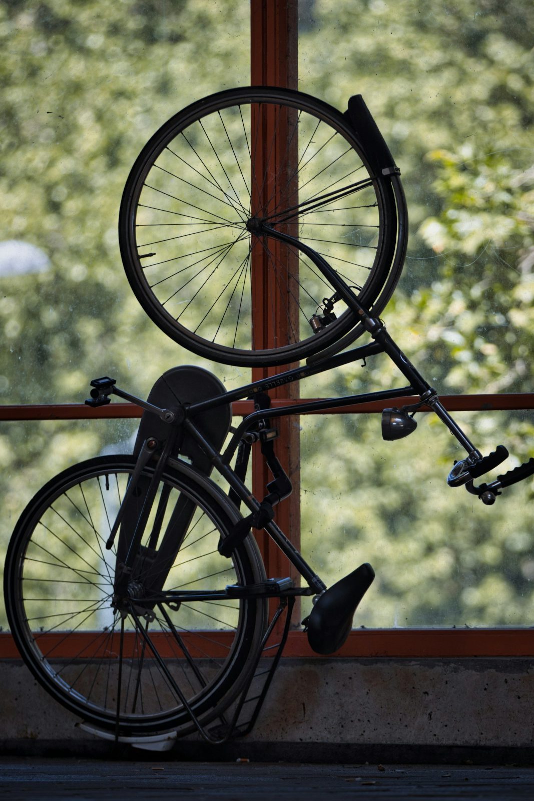 Bicycle hung by its front wheel on a wall hook in front of a window