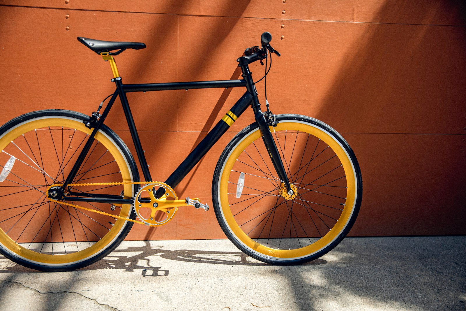 Black single-speed bike with yellow rims leaning on an orange wall