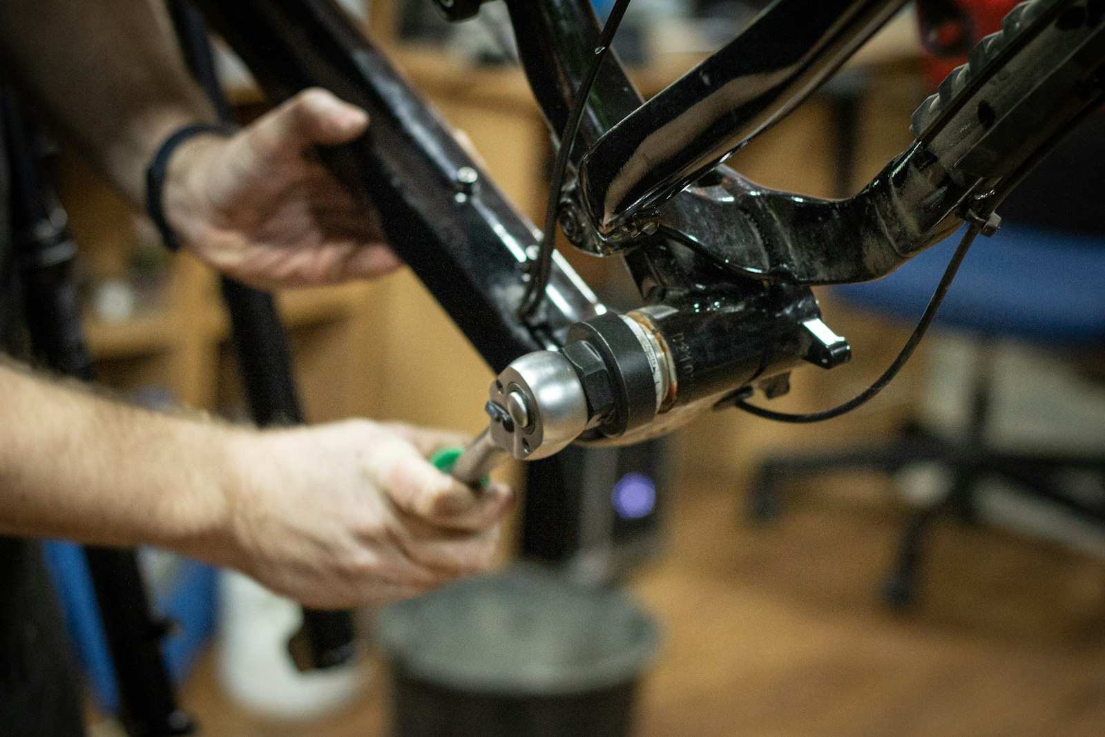 Two hands tightening a bottom bracket with a tool, bike frame upside down in a workstand