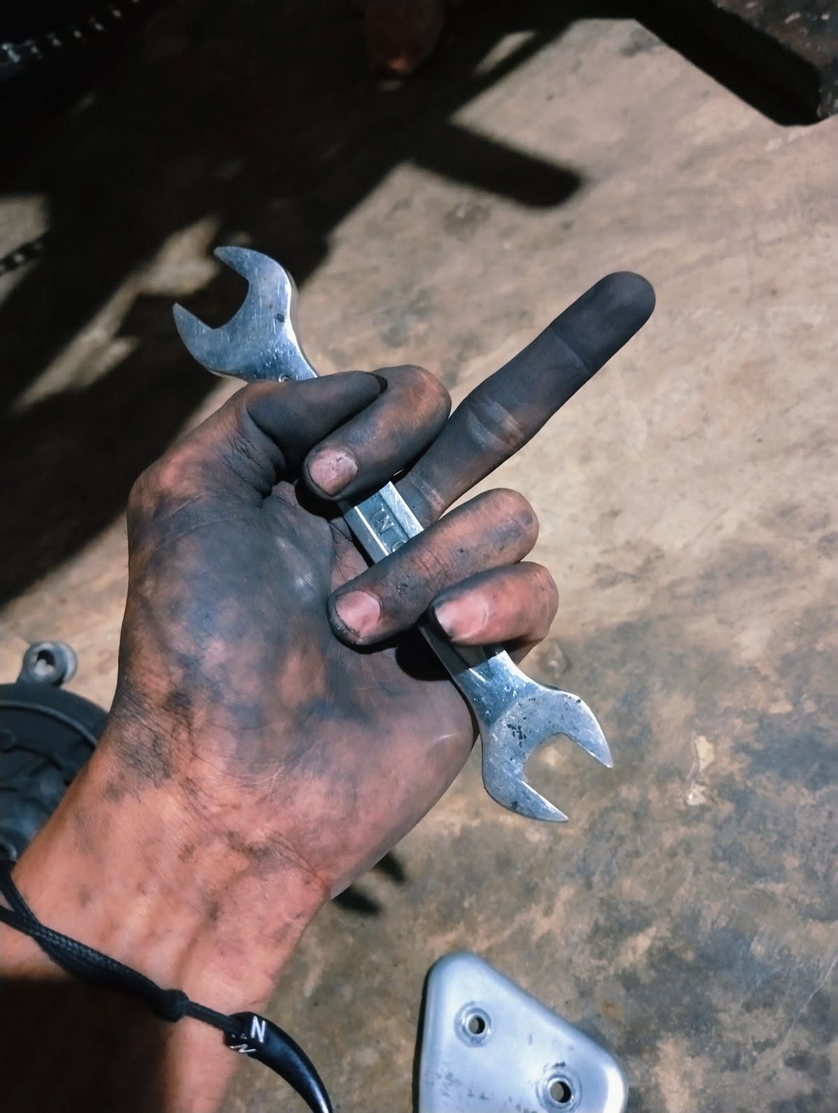 Oil-blackened hand holding an open-ended spanner over a concrete floor