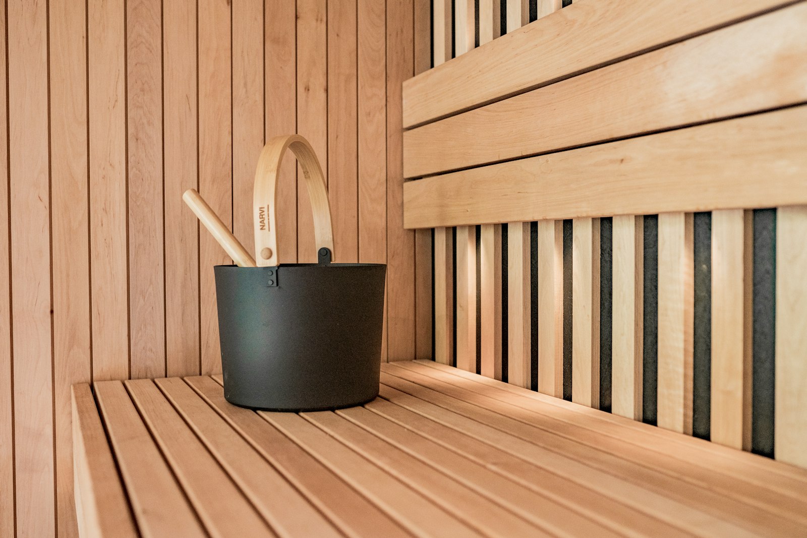 Black bucket and wooden ladle on a pale sauna bench