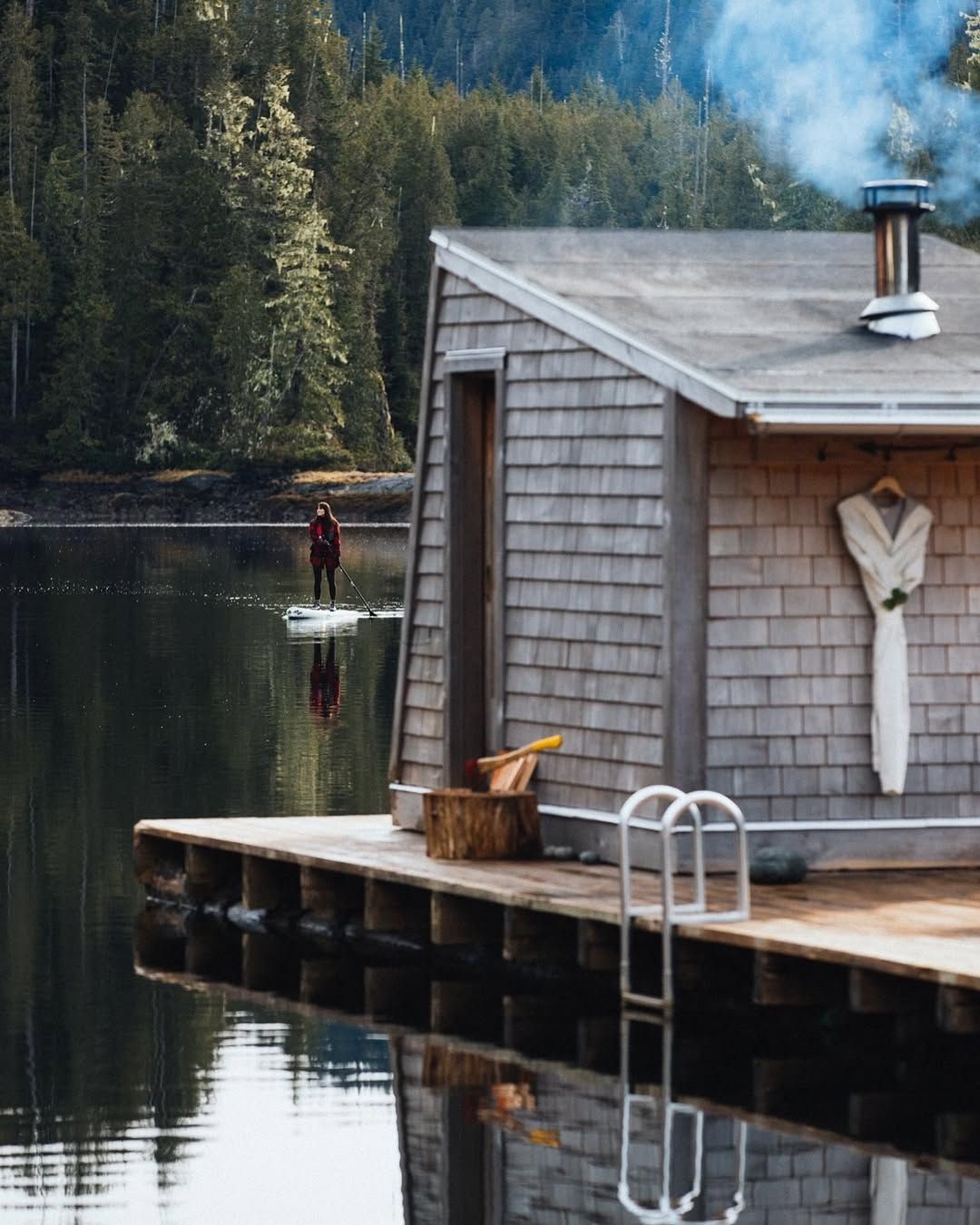 Shingled sauna house on a floating jetty with smoke from the chimney