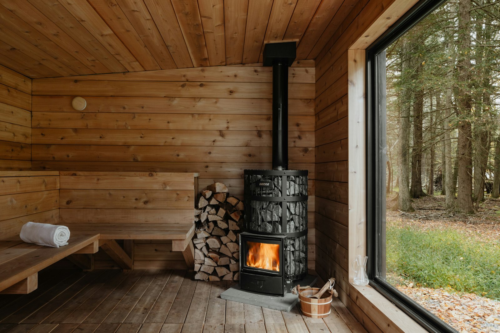 Wood stove burning in a timber sauna room with a window onto birch trees