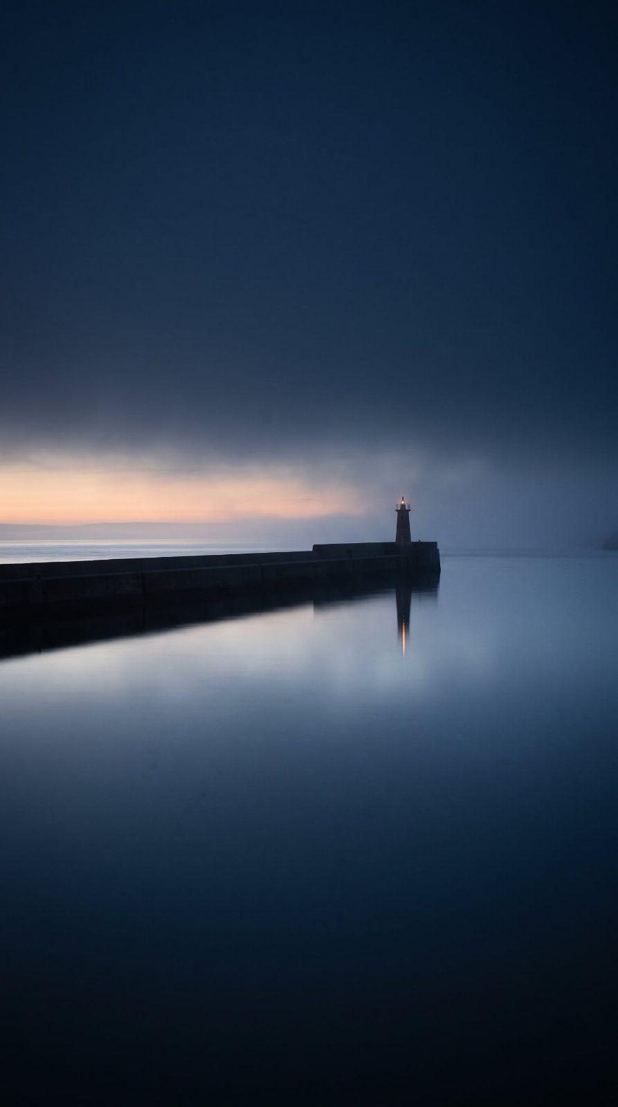 A breakwater light at dusk over still water