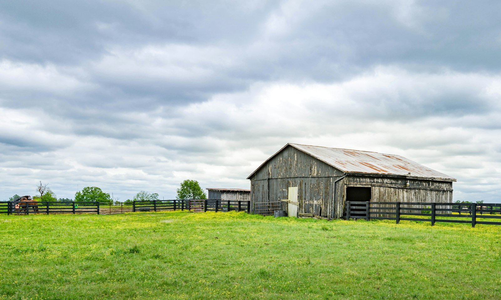 Grey timber barn in a green field under an overcast sky