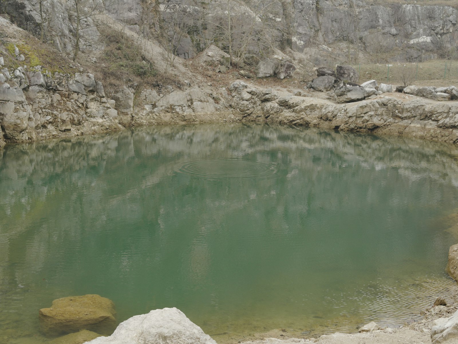 Flooded pit below grey limestone ledges