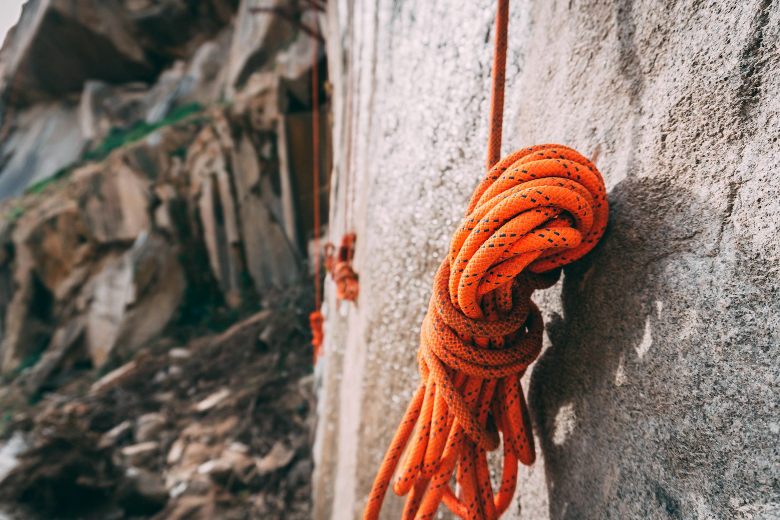 A coiled orange rope hanging against a grey rock wall