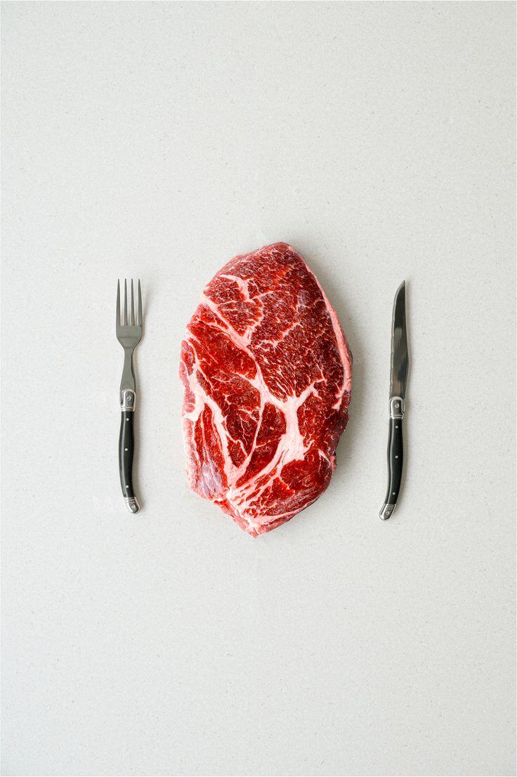 Marbled beef steak on a white board between a fork and a knife