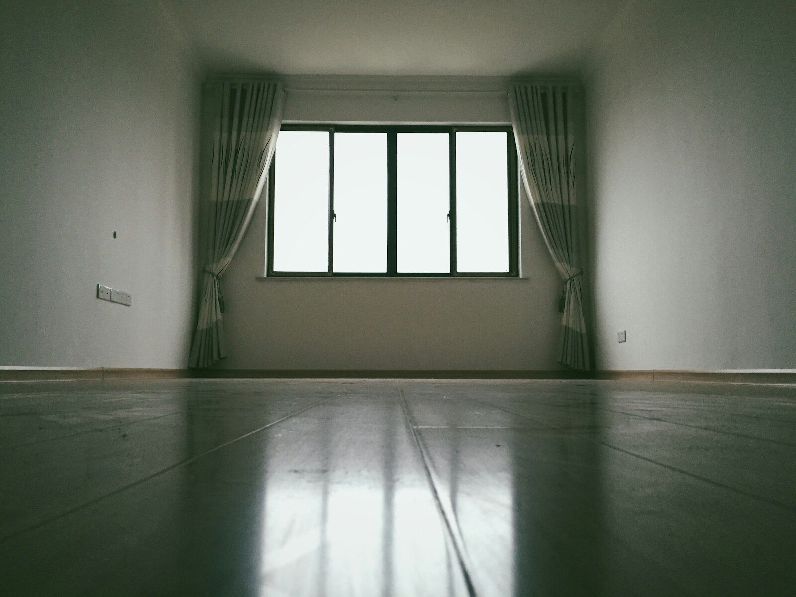 Empty room with one window and long curtains, floor still reflecting the light