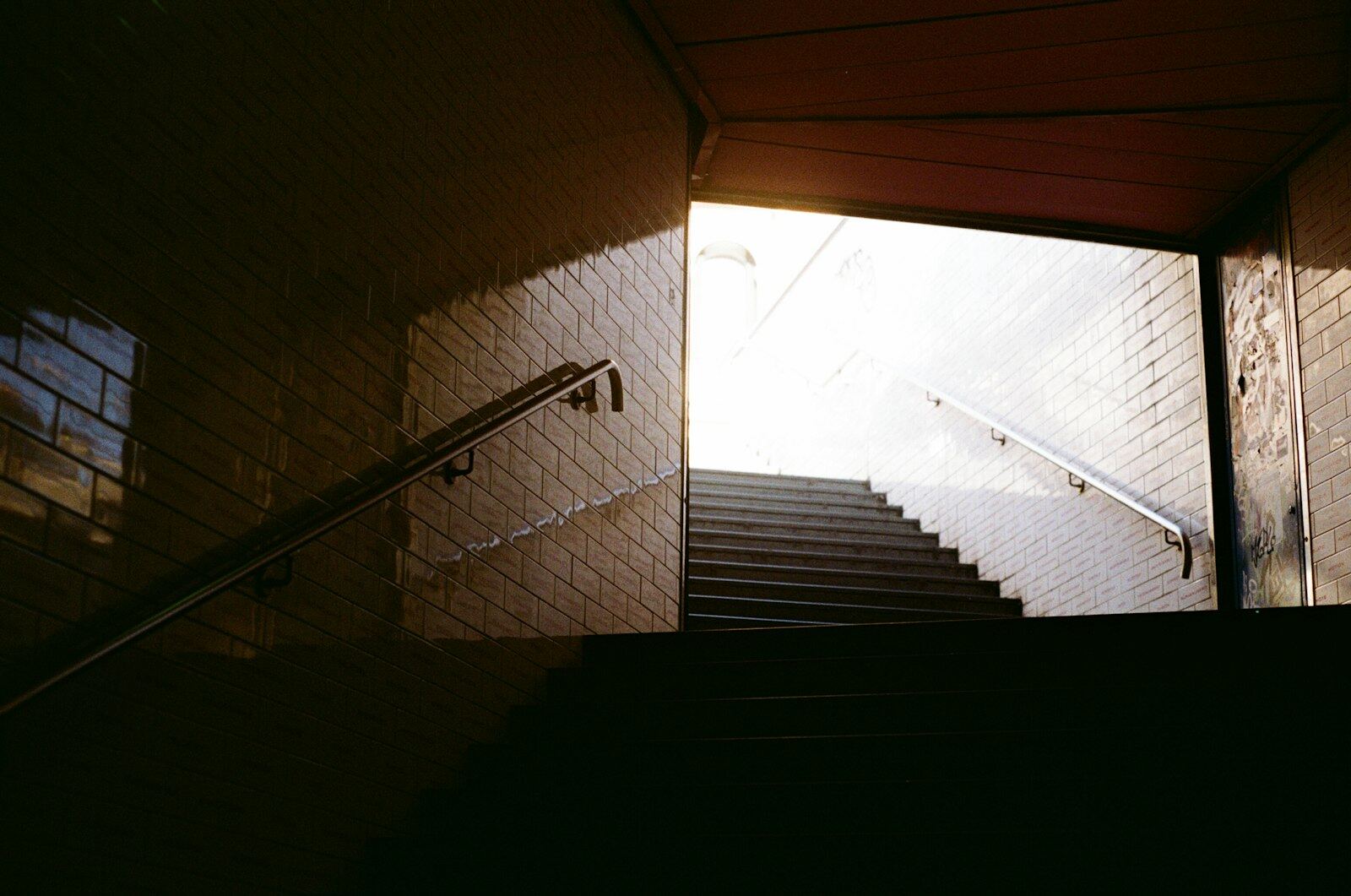Tiled stairwell rising to daylight, handrail on the left